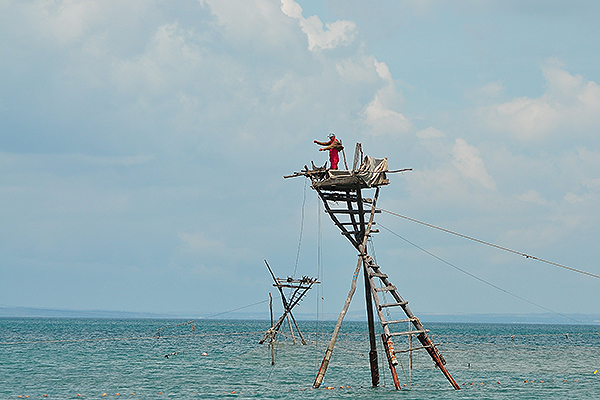 Рыбак на караве (сети с опорами для ловли рыбы, стоящие в море) высматривает рыбу. Фото: Элина Мятыга / «Русская планета»